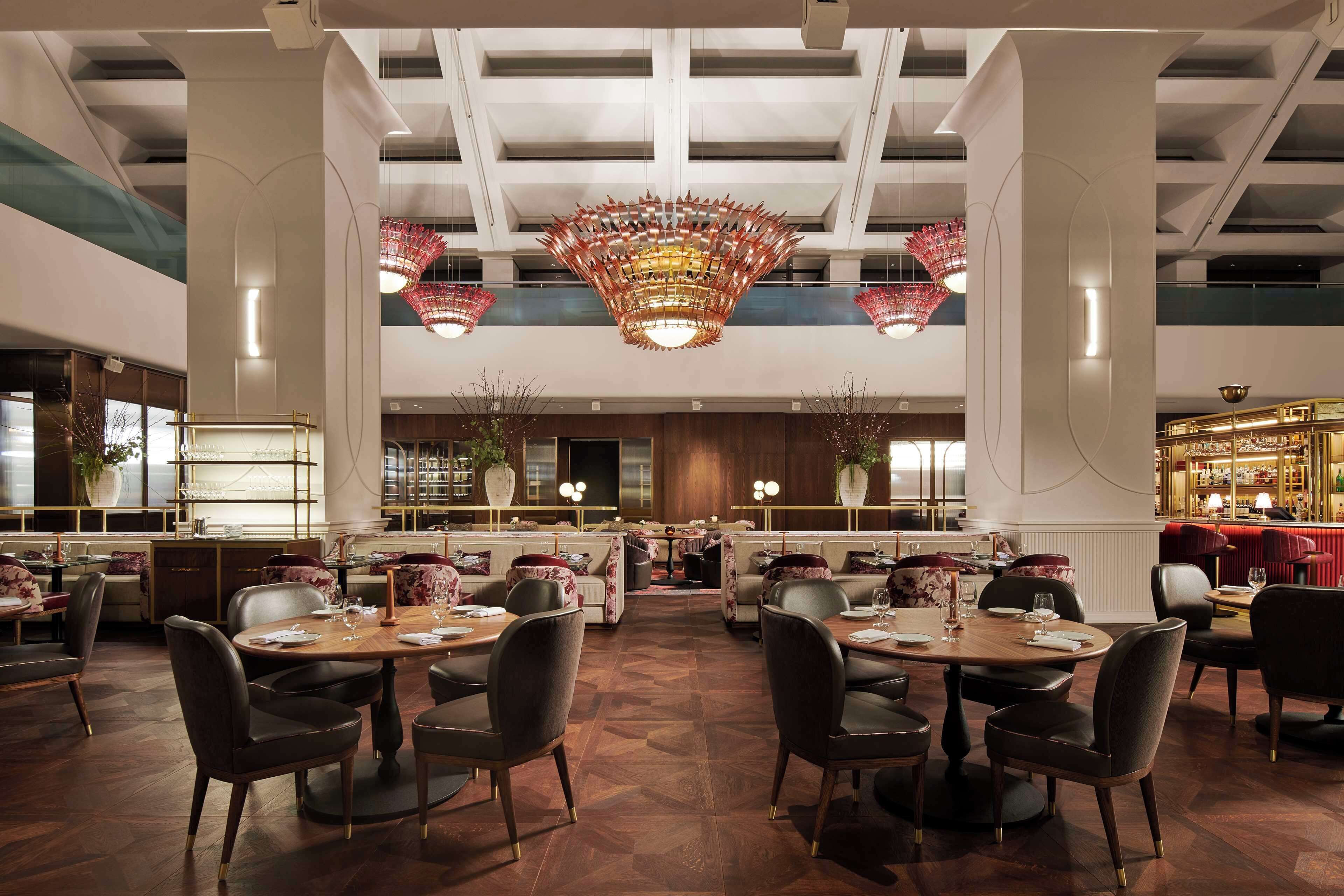 Un restaurante espacioso con techos altos, candelabros modernos y una zona de bar central.