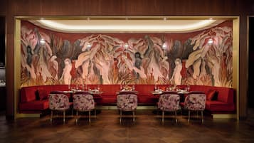 A restaurant with a red sofa and floral chairs, a large abstract mural on the wall, and a wooden floor.