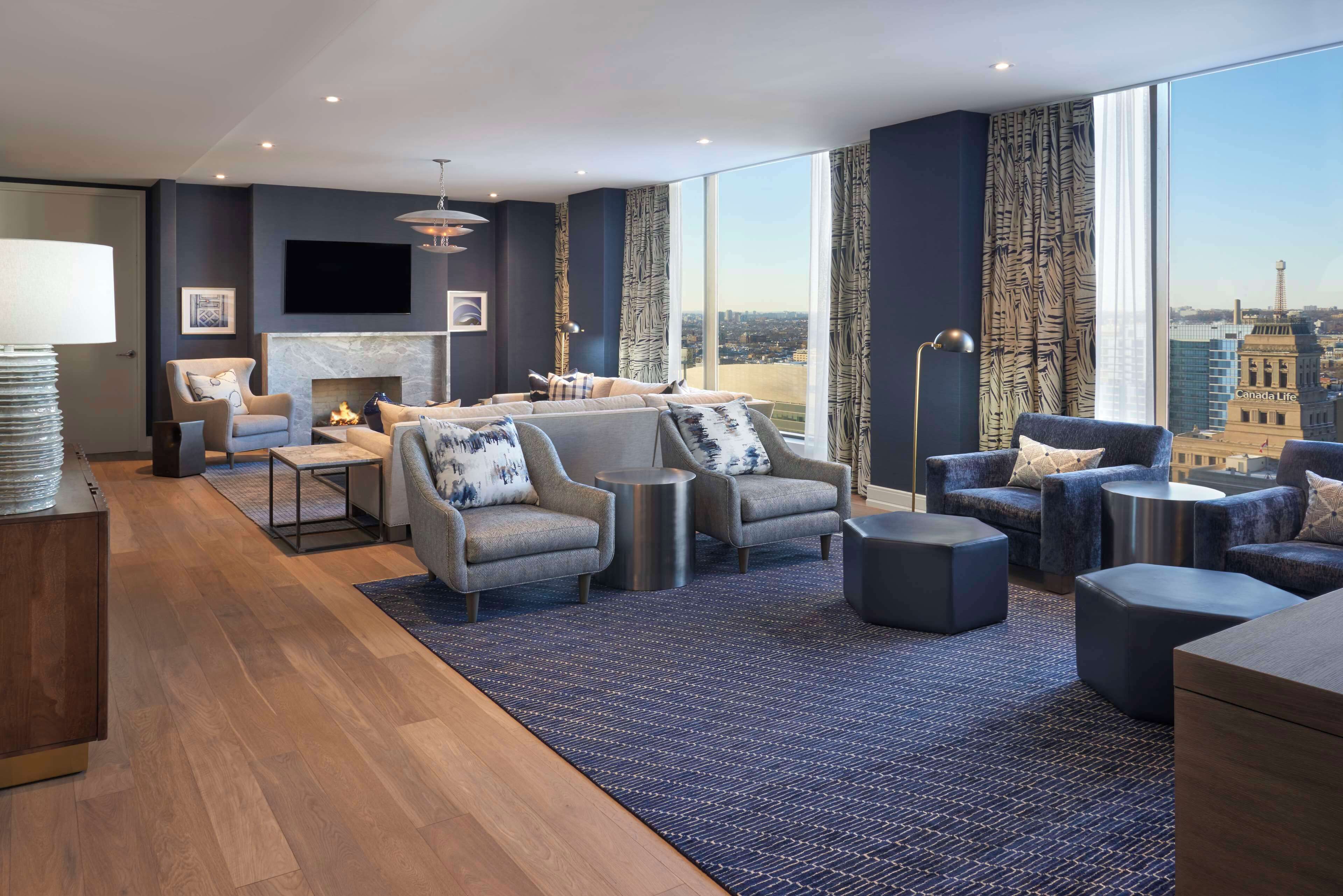 A modern living room with a fireplace, comfortable seating, and a large window offering a city view.