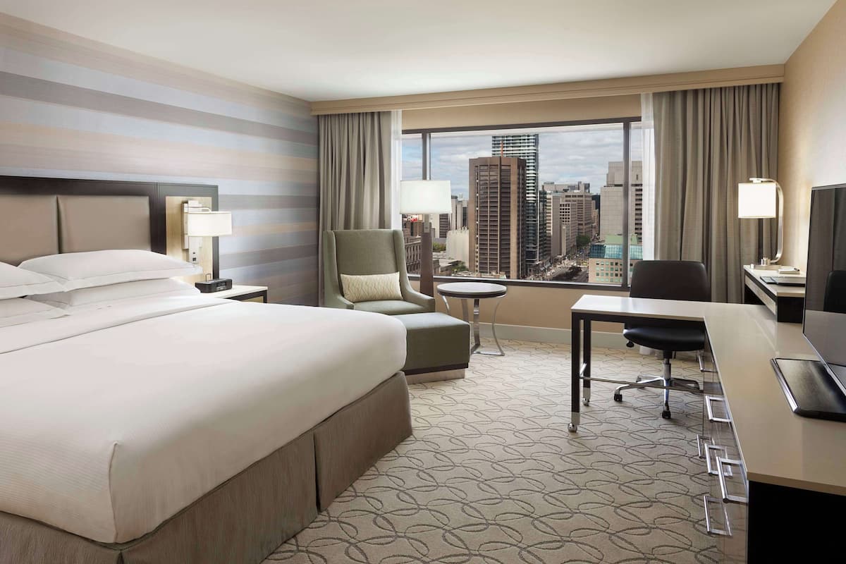 A hotel room with a large bed, a desk, a chair, a small table, and a TV.