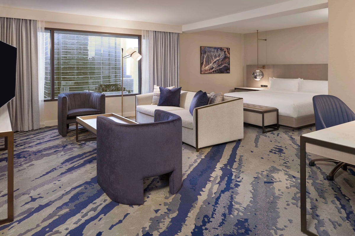 A hotel room with a large window, a sofa, a desk, and a bed.
