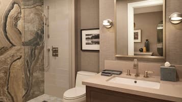 A modern bathroom with a marble wall, a toilet, a sink with a mirror, and a shower.