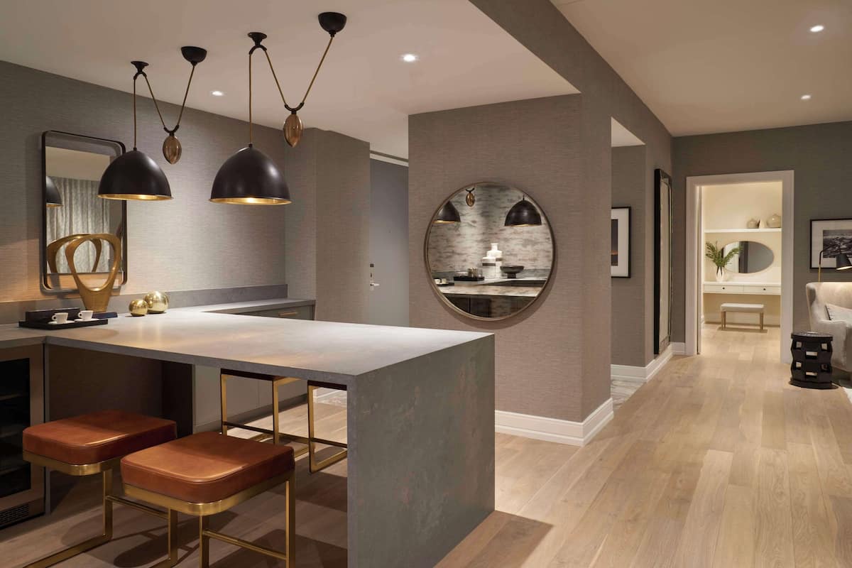 A modern kitchen with a central island, bar stools, pendant lighting, and a round mirror on the wall.