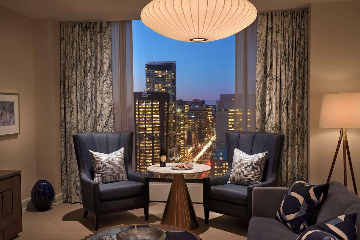 A modern living room with two armchairs, a coffee table, and a view of a cityscape at dusk.