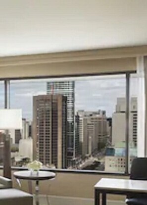 A modern hotel room with a large window offering a city view. There are two tables, one with a vase of flowers. - Hilton Toronto (Toronto)