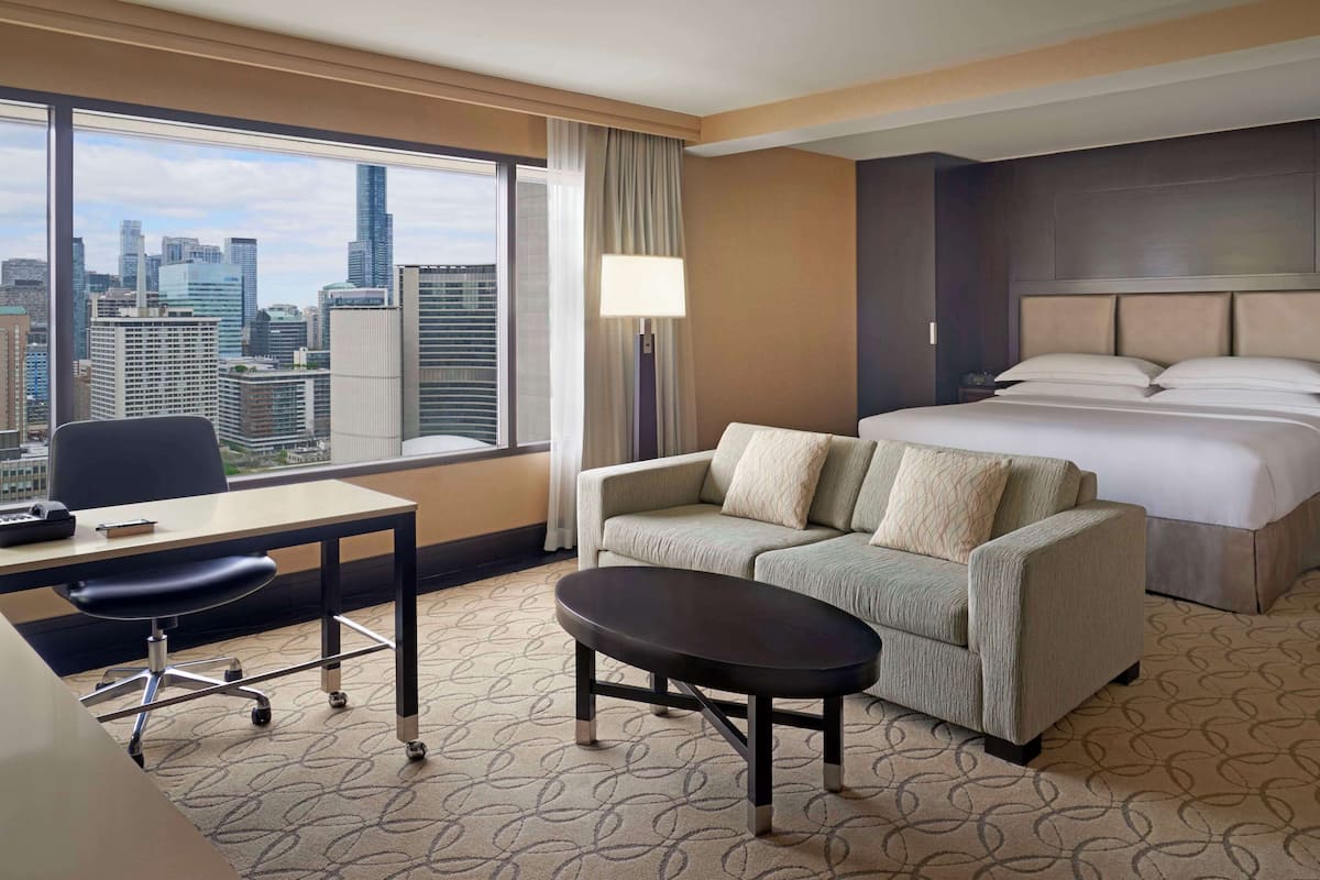 A hotel room with a city view, a desk with a chair, a sofa, a bed, and a small table.