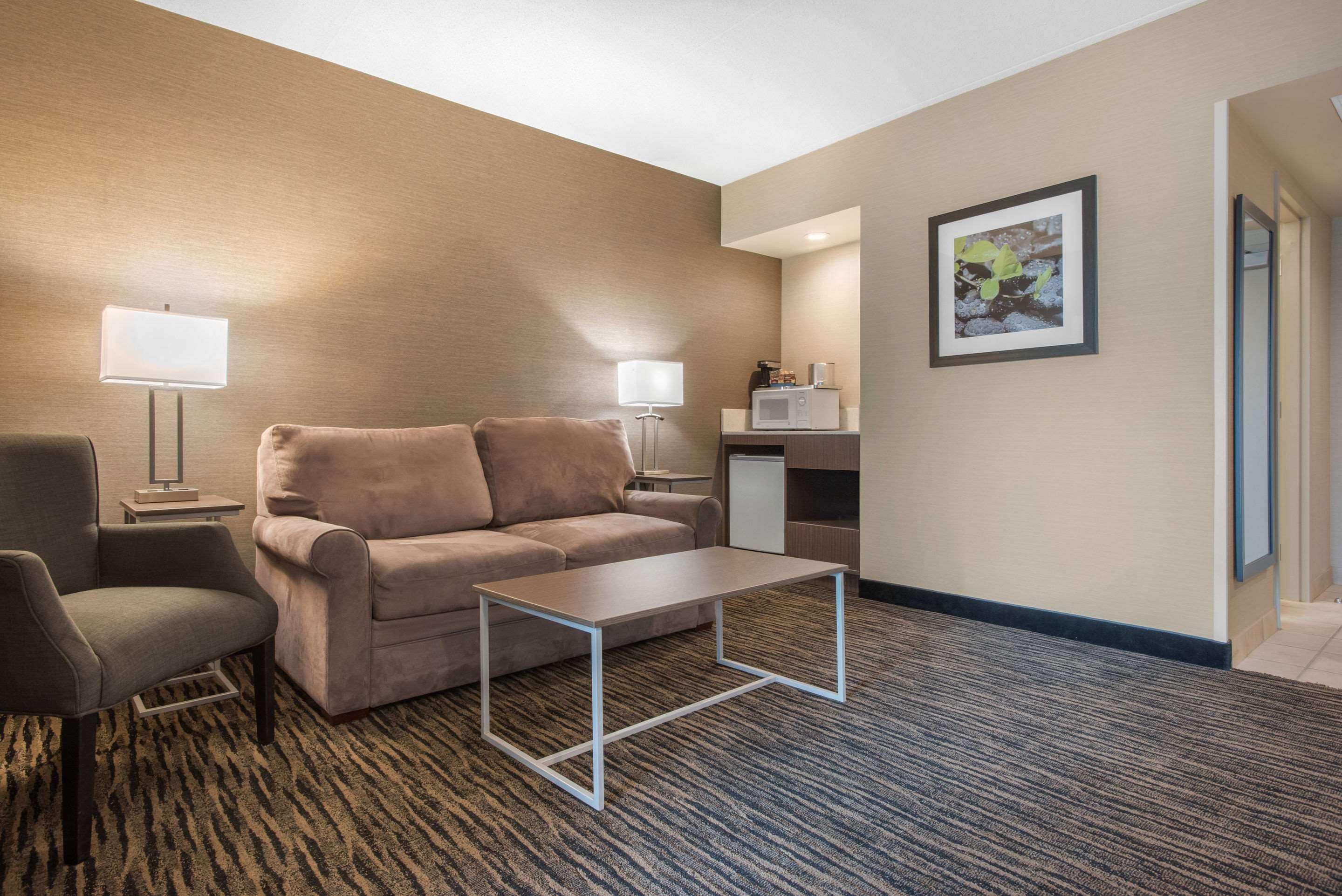 A hotel room with a sofa, a small table, a lamp, a microwave, and a framed picture on the wall.