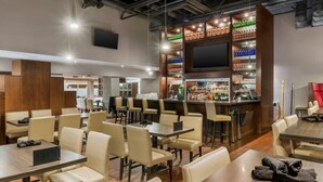 Un restaurante con varias mesas y sillas, una zona de bar con estantes llenos de botellas y un televisor de pantalla plana montado en la pared.