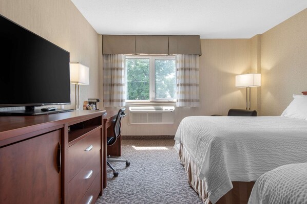 Habitación de hotel con cama, escritorio con silla, televisor, ventana con cortinas y lámpara.