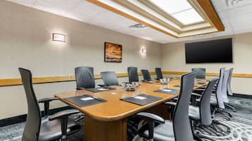 A conference room with a long table, multiple chairs, a projector screen, and a painting on the wall.