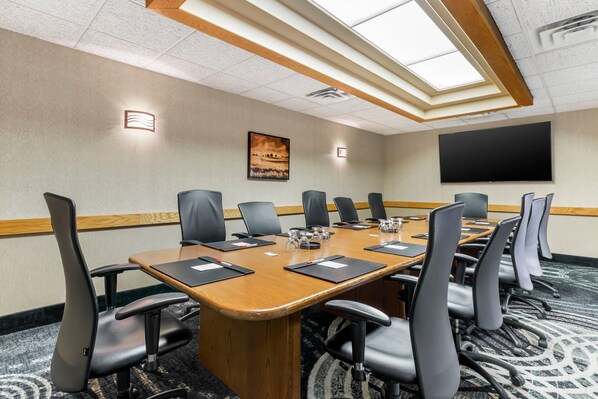 A conference room with a long table, multiple chairs, a projector screen, and a painting on the wall.