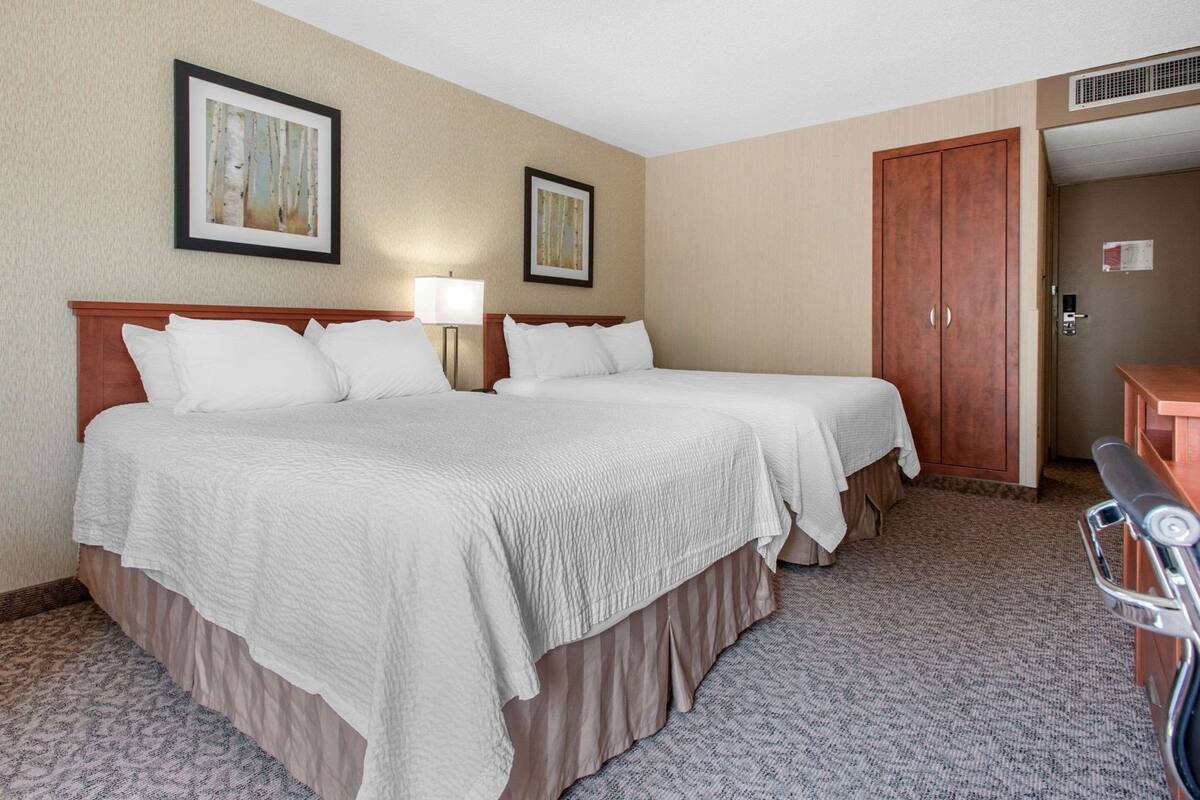 A hotel room with two beds, a desk, a wardrobe, and two framed pictures on the wall.