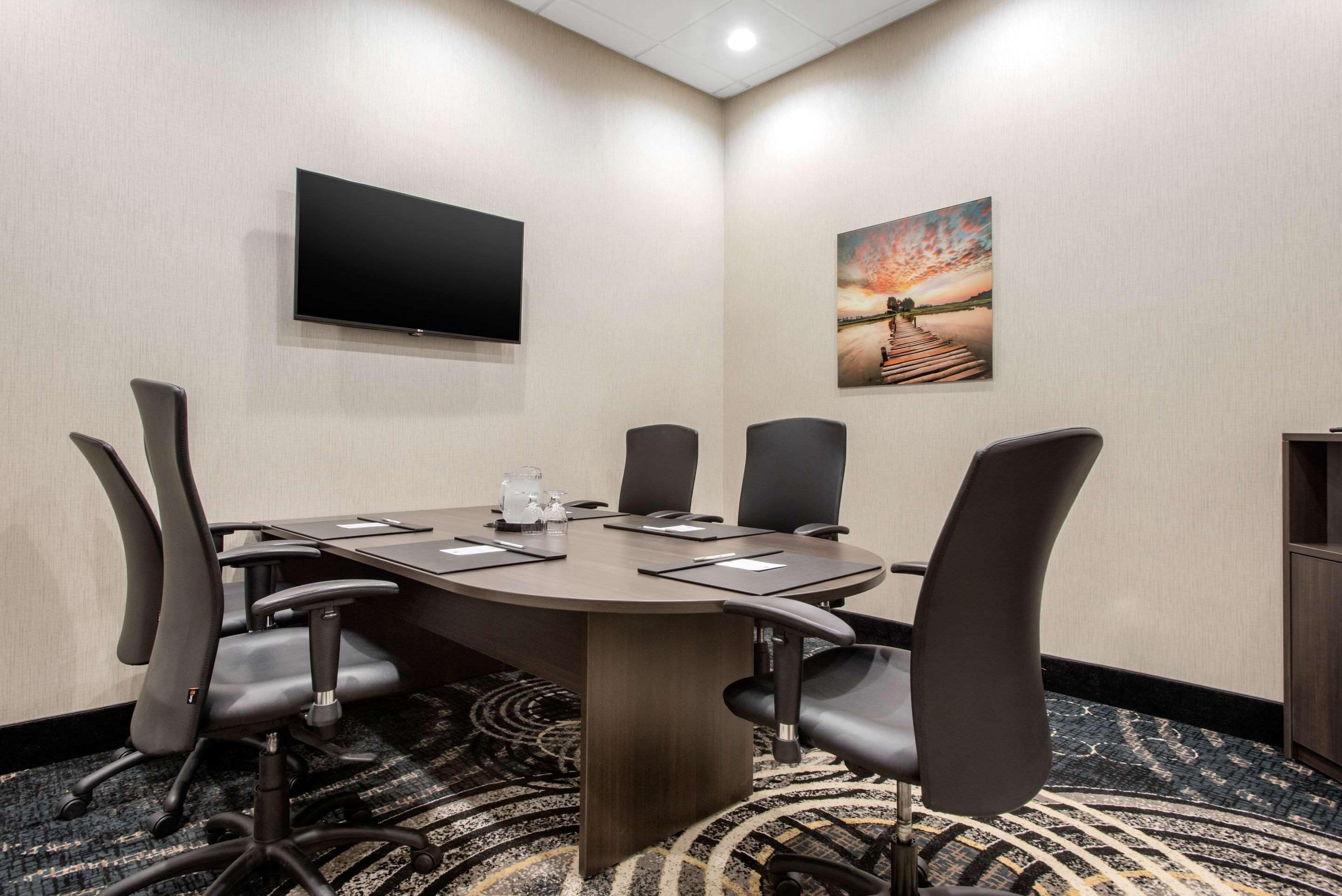 A conference room with a large table, six chairs, a flat-screen TV, and a painting on the wall.