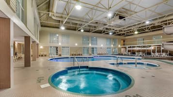 An indoor swimming pool with multiple lanes, a high ceiling with visible beams, and a tiled floor with directional arrows.