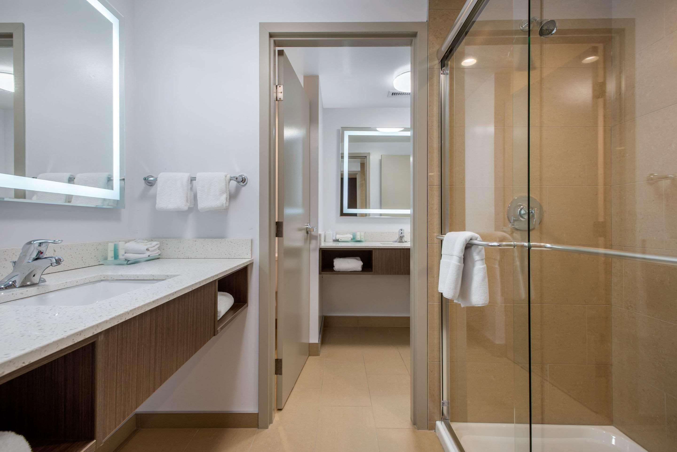 Un baño moderno con cabina de ducha de vidrio, un espejo grande y un lavabo con artículos de aseo.