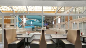 A restaurant with high tables and cushioned booths, large windows with a view of a water slide and outdoor seating area. - Superior Inn Hotel and Conference Centre Thunder Bay (Thunder Bay)