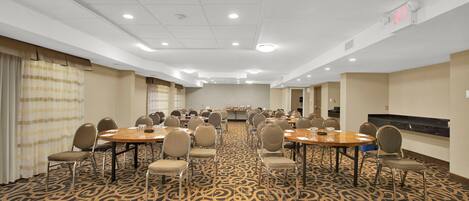 Un salón de conferencias con varias mesas y sillas, una alfombra estampada e iluminación empotrada en el techo.