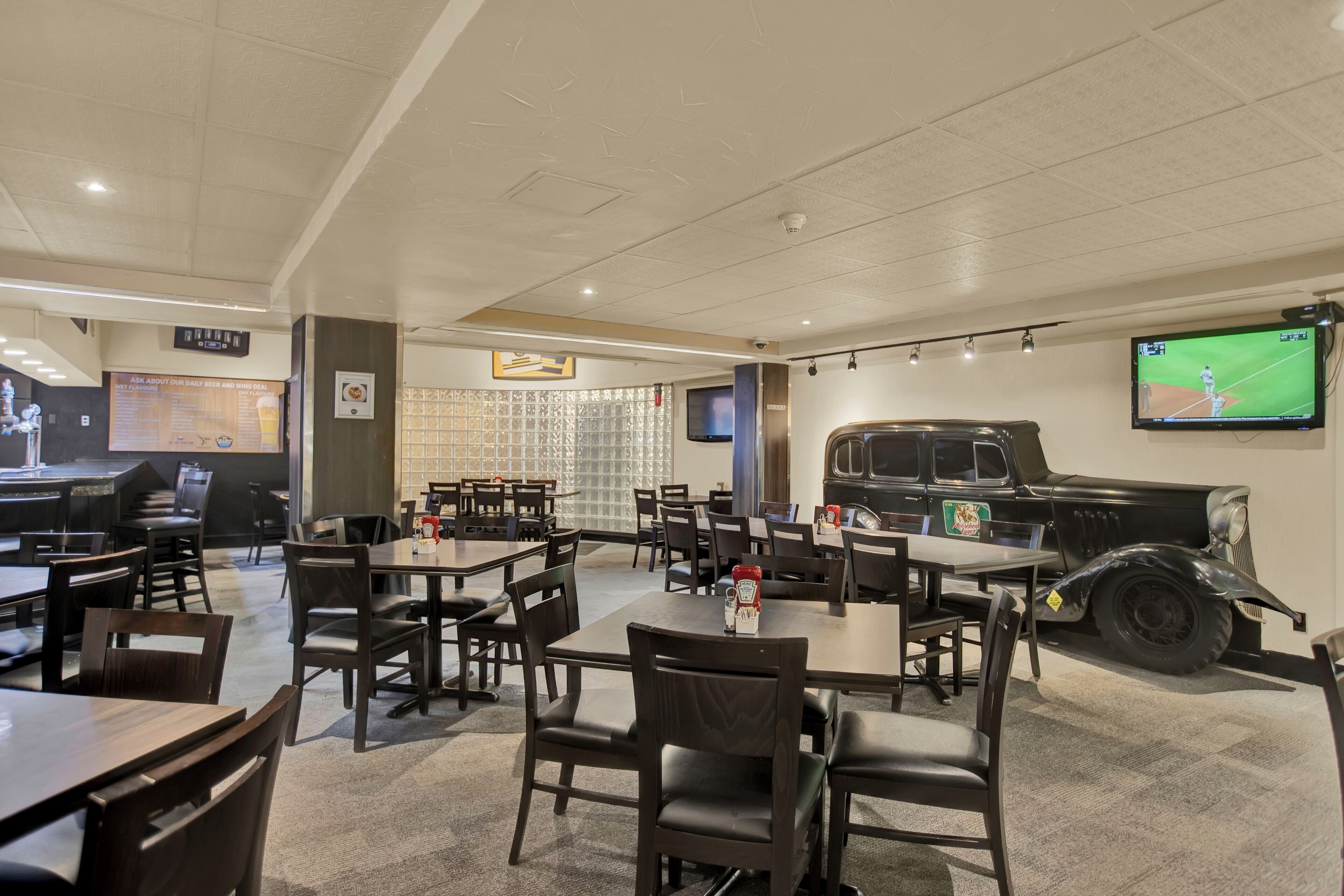 Un restaurante con mesas y sillas, un televisor en la pared y un modelo de coche antiguo.