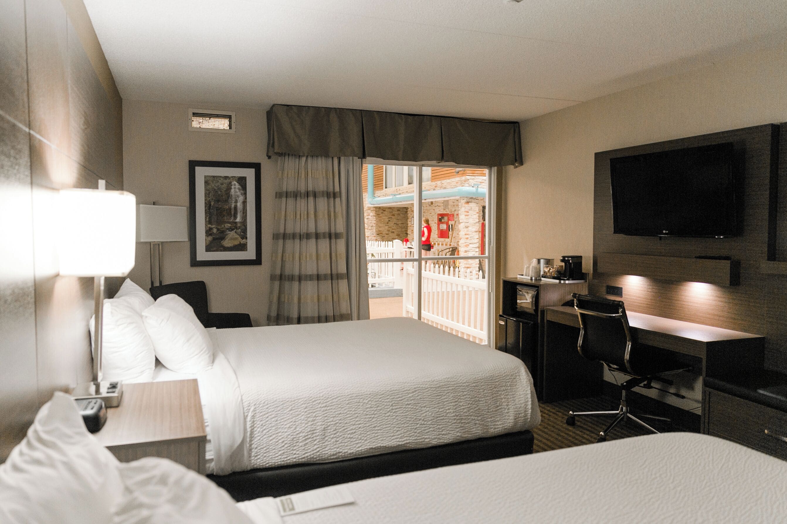 Habitación de hotel con cama, escritorio, silla, televisor y balcón con vistas.