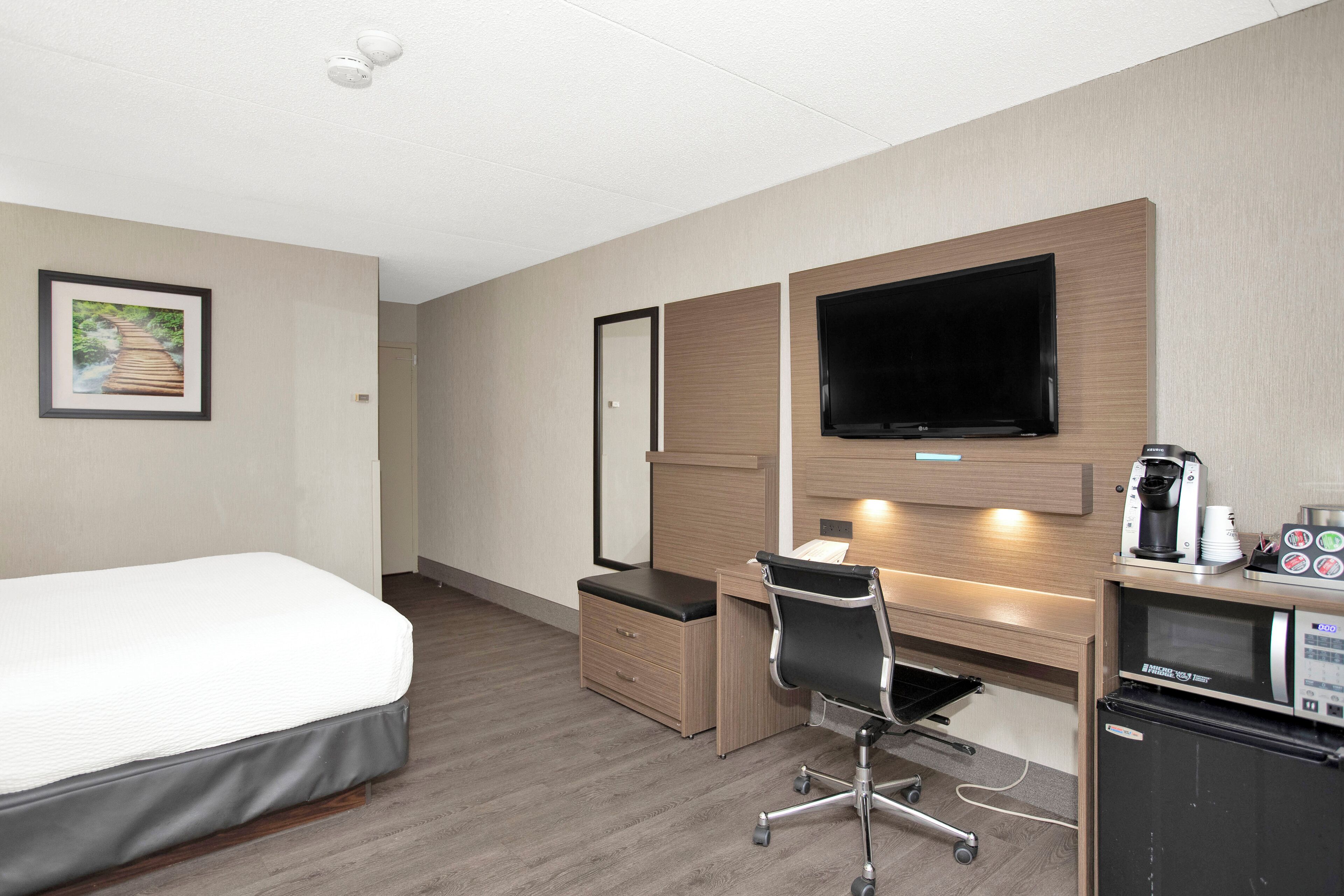 A hotel room with a bed, a desk with a chair, a television, a coffee machine, and a microwave.