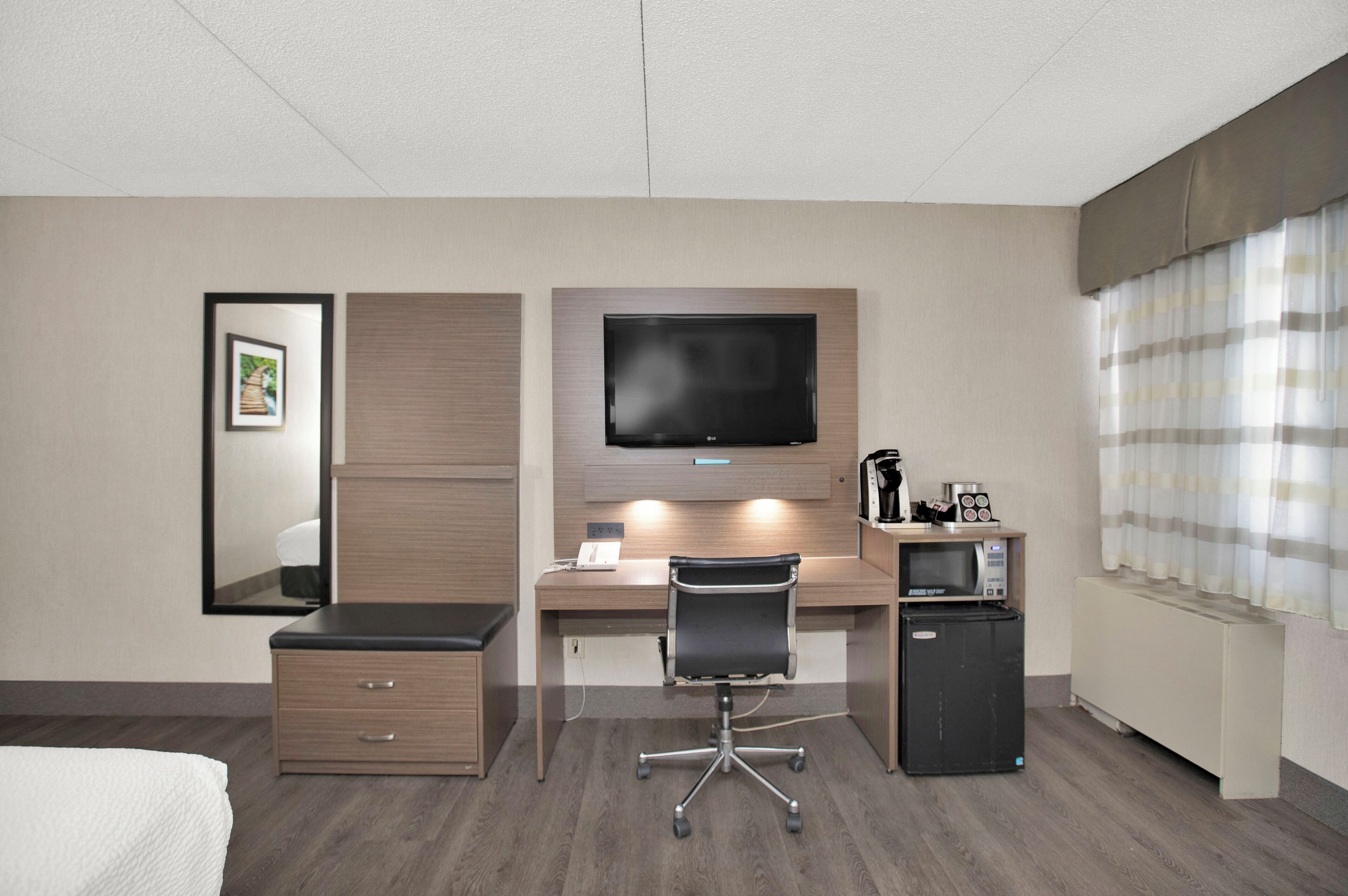A hotel room with a bed, a desk with a chair, a television, a mini-fridge, and a microwave.