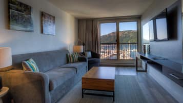Een moderne woonkamer met een grijze bank, een houten salontafel en een grote televisie. Twee schilderijen hangen aan de muur en er is een balkon met uitzicht op zee.