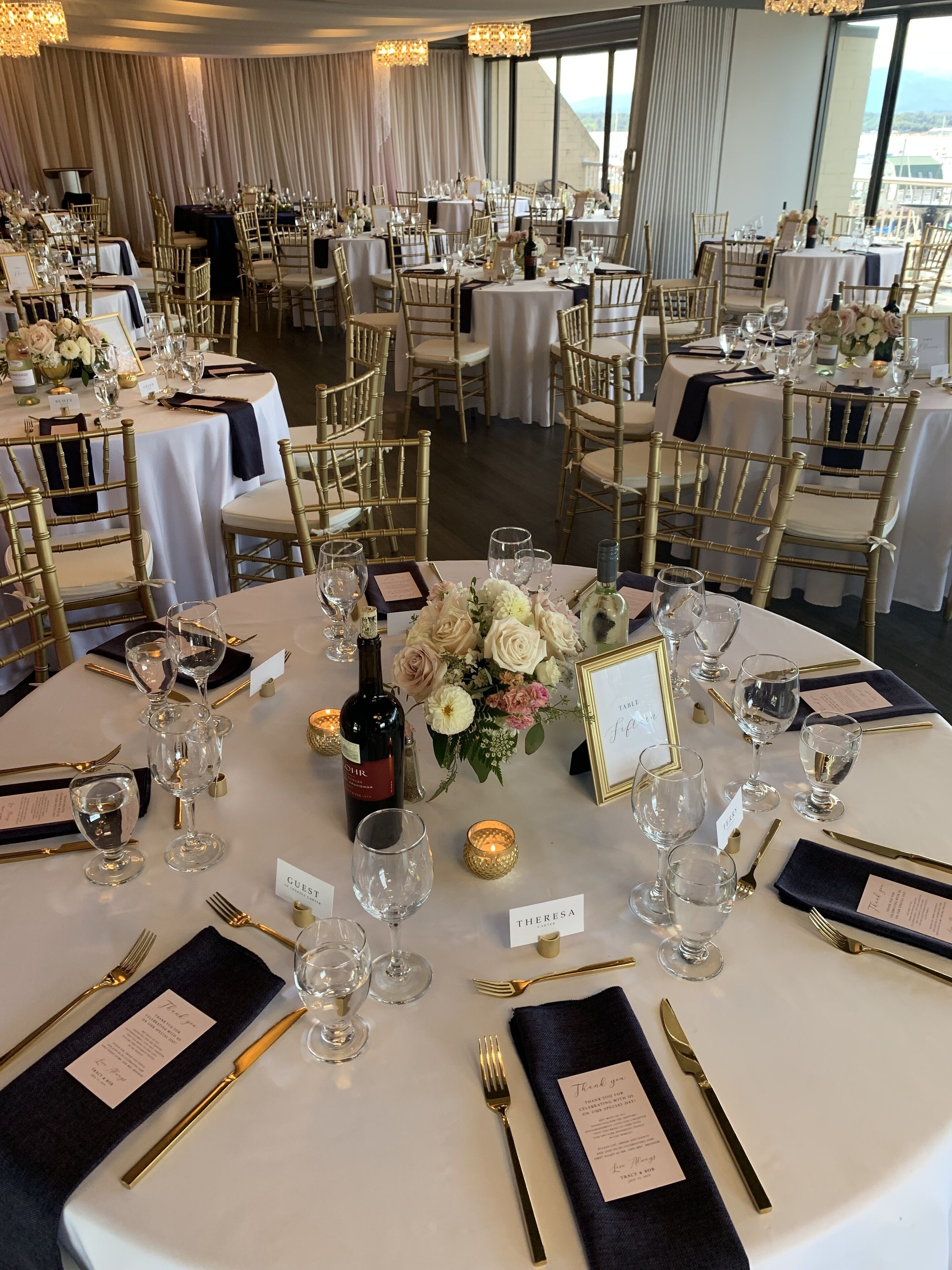Un salón de banquetes con mesas redondas, sillas doradas y manteles blancos.