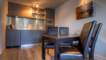A modern kitchen with dark cabinetry, a microwave, and a coffee maker. There is a dining table with two chairs and a painting on the wall.