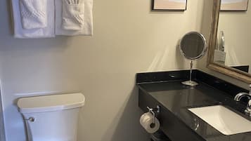 Un baño con inodoro, lavamanos, espejo y repisa con toallas.