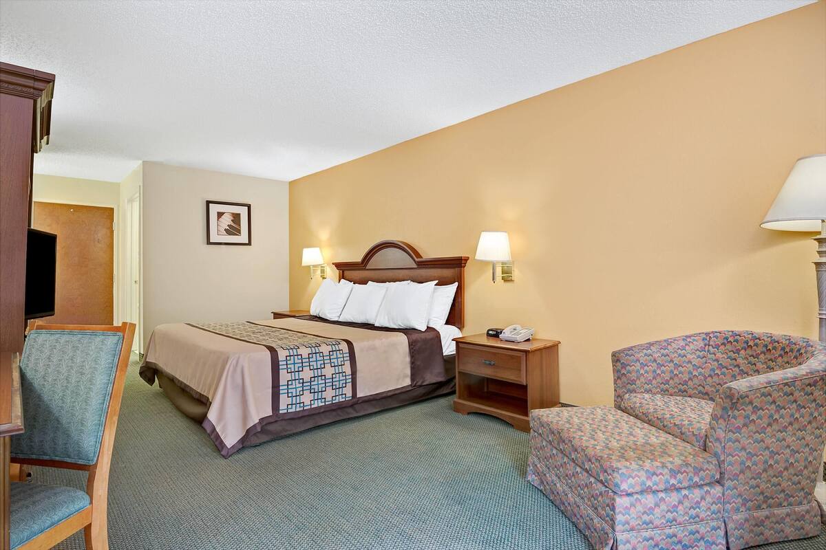 A hotel room with a bed, bedside table, chair, and a lamp.