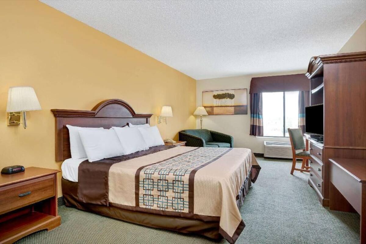 A hotel room with a bed, bedside tables, a desk, a chair, a TV, and a window with curtains.