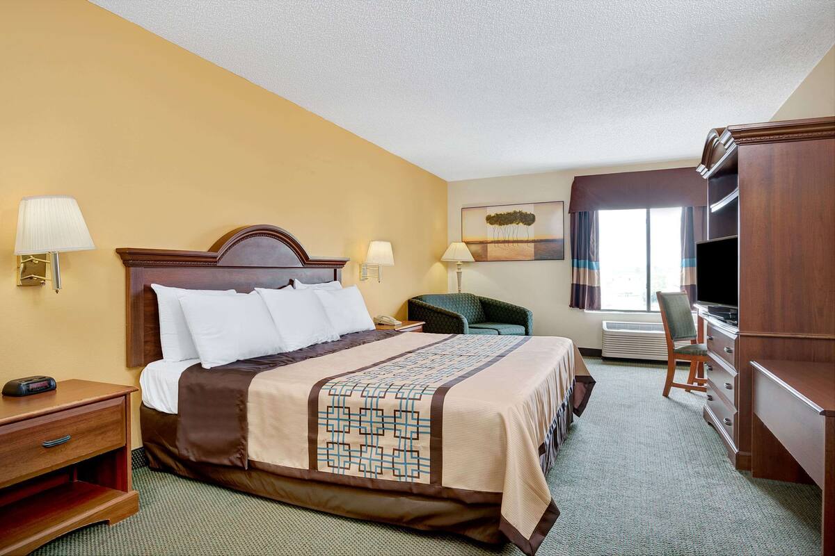 A hotel room with a large bed, bedside lamps, a desk, a chair, a TV, and a dresser.