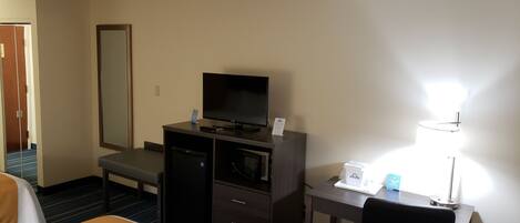 A hotel room with a bed, a desk, a television, a trash bin, and a lamp.