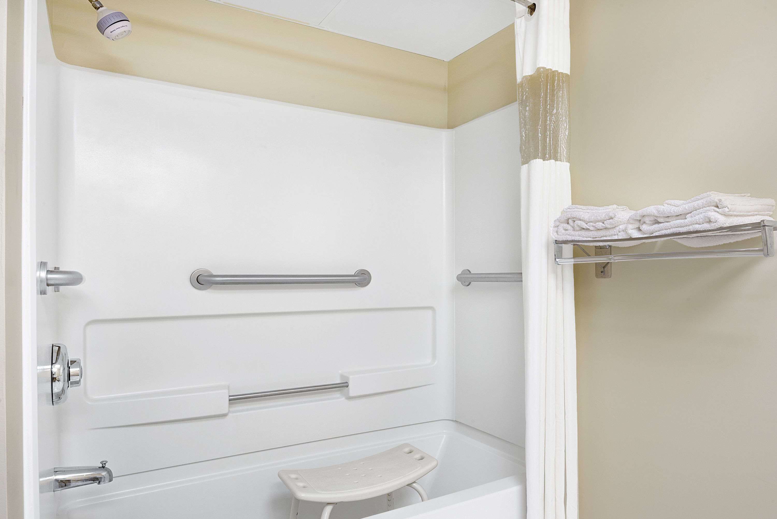 A bathroom with a white bathtub, grab bars, a shower curtain, and a towel rack.
