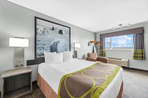 Habitación de hotel con una cama grande, una mesita de noche, una silla, un escritorio, una ventana con cortinas y un aire acondicionado instalado en la pared.