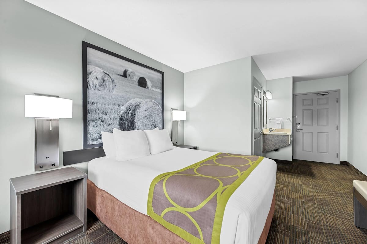 A hotel room with a large bed, two bedside tables, a nightstand, a wall-mounted TV, a bathroom with a sink and mirror, and a door.