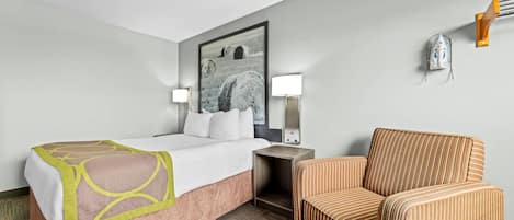 Habitación de hotel con cama, una silla, una mesita de noche, una lámpara y un planchador de pared.