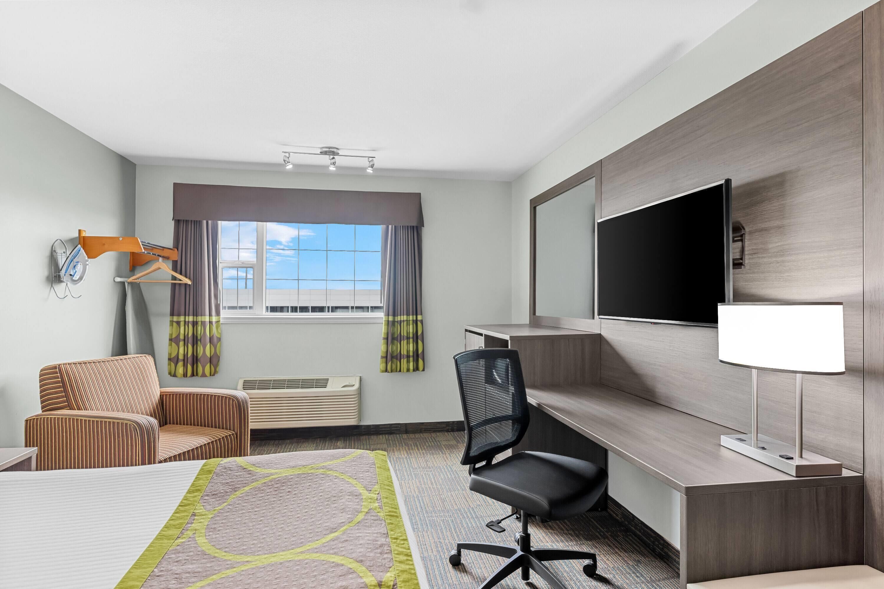 A hotel room with a bed, a desk, a chair, a TV, and a window with curtains.
