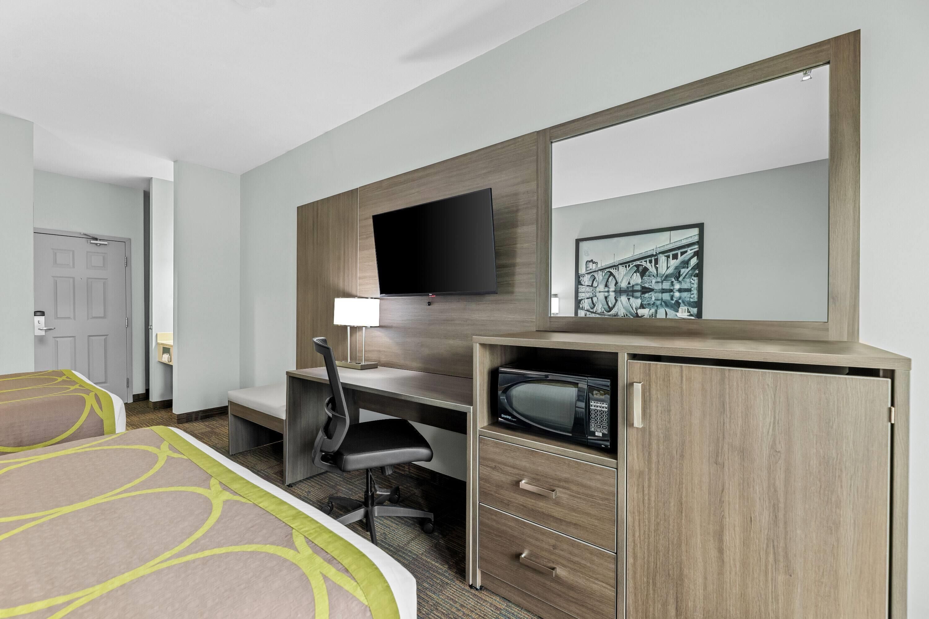 Een hotelkamer met een bed, bureau, stoel, televisie, magnetron en een grote spiegel.
