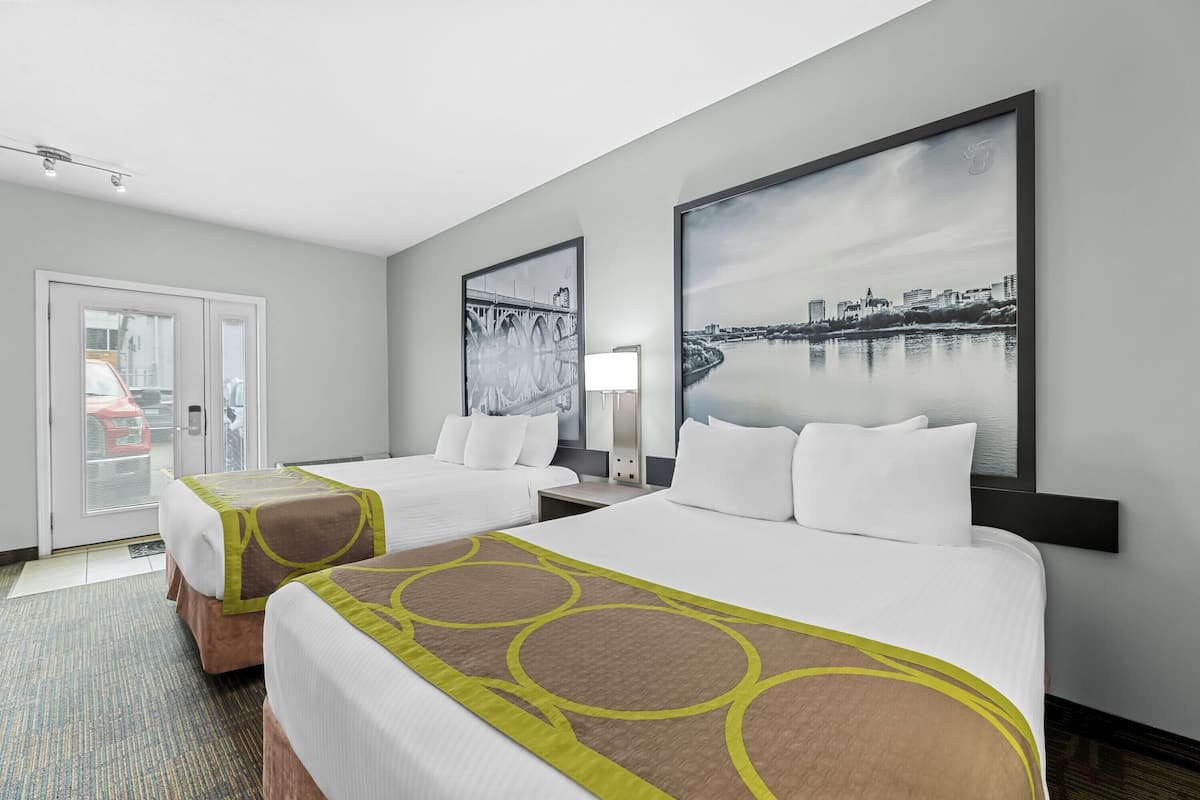 A hotel room with two beds, a cityscape view, and a door leading to a balcony.