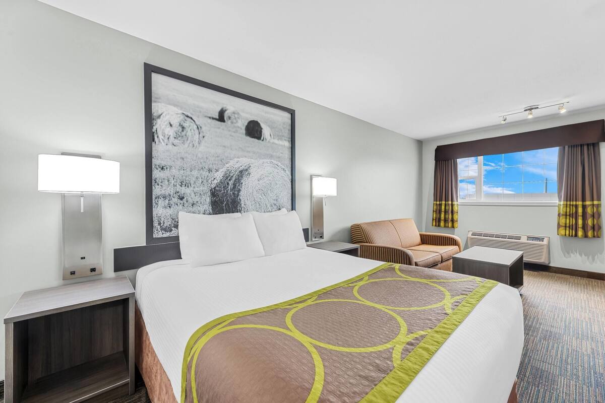 A hotel room with a large bed, two bedside tables, a chair, a desk, and a large window with curtains.