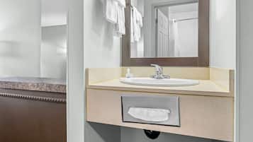 Un baño con lavamanos, espejo, toallero y dispensador de toallas.