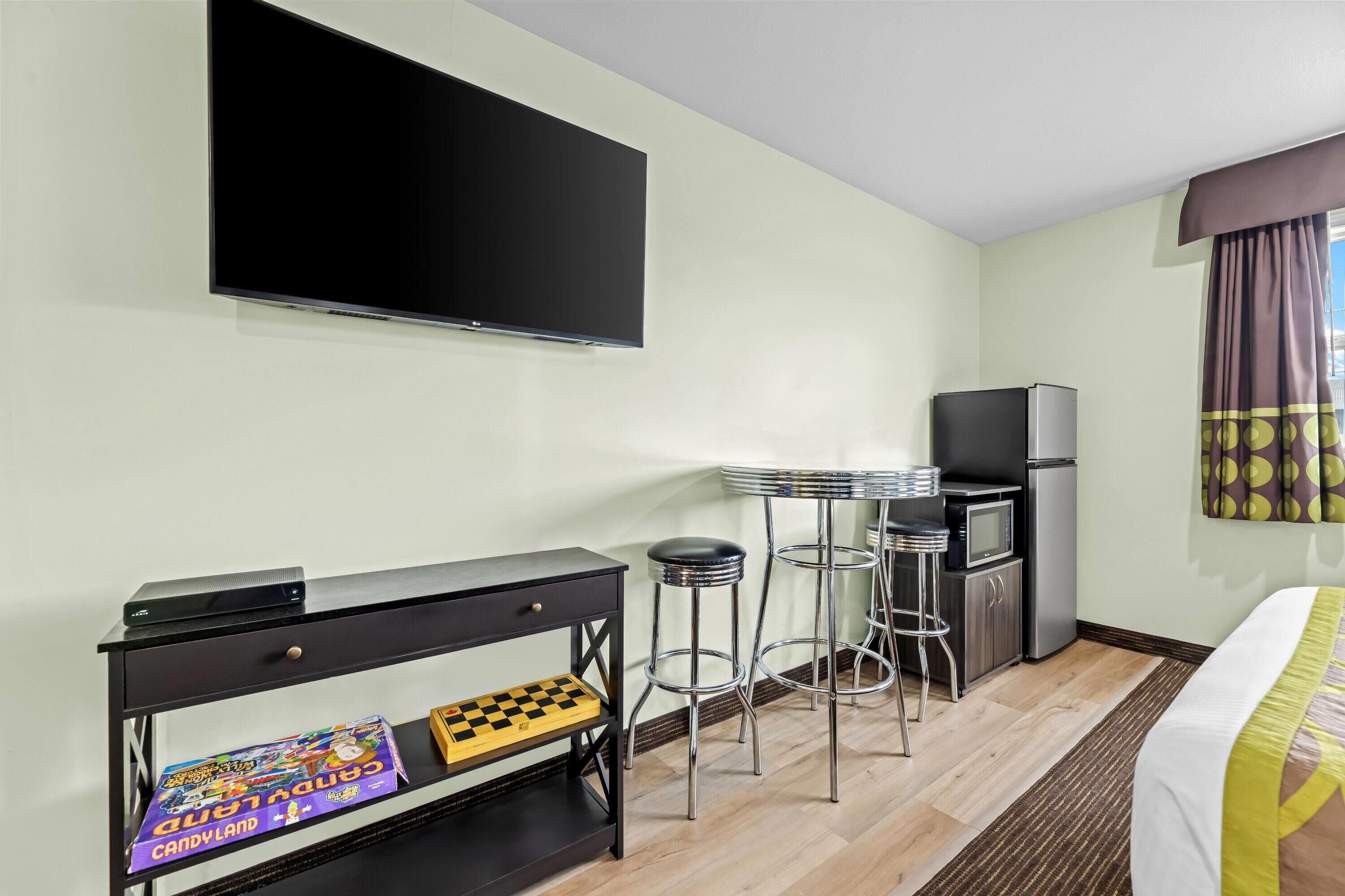 Habitación de hotel con televisión de pantalla plana, un escritorio pequeño con un tablero de ajedrez, un refrigerador y una cama con colcha a rayas.