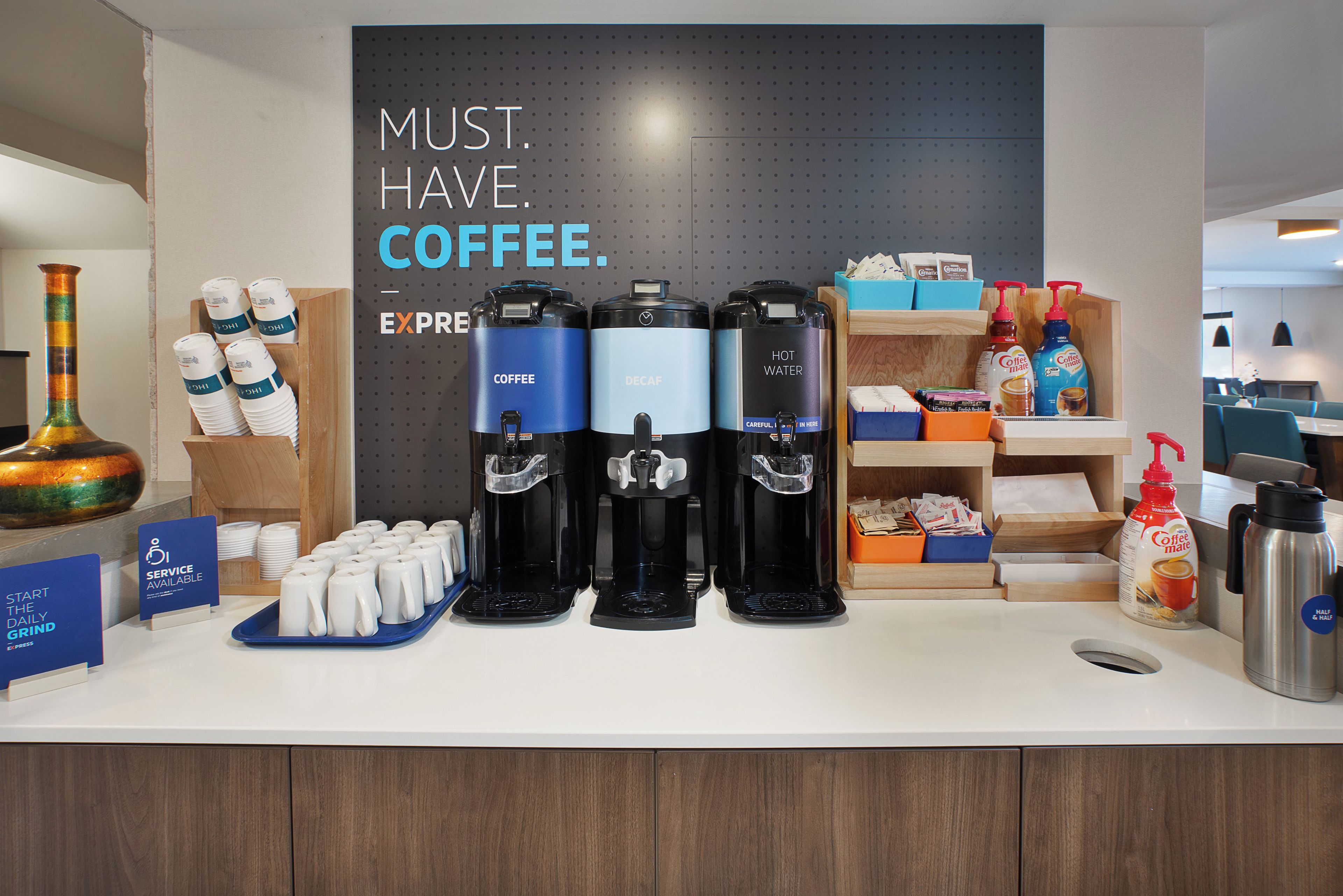 Un espace dédié au café, équipé de plusieurs distributeurs de café, d’une machine à café et d’un panneau indiquant : « IL FAUT ABSOLUMENT DU CAFÉ ».