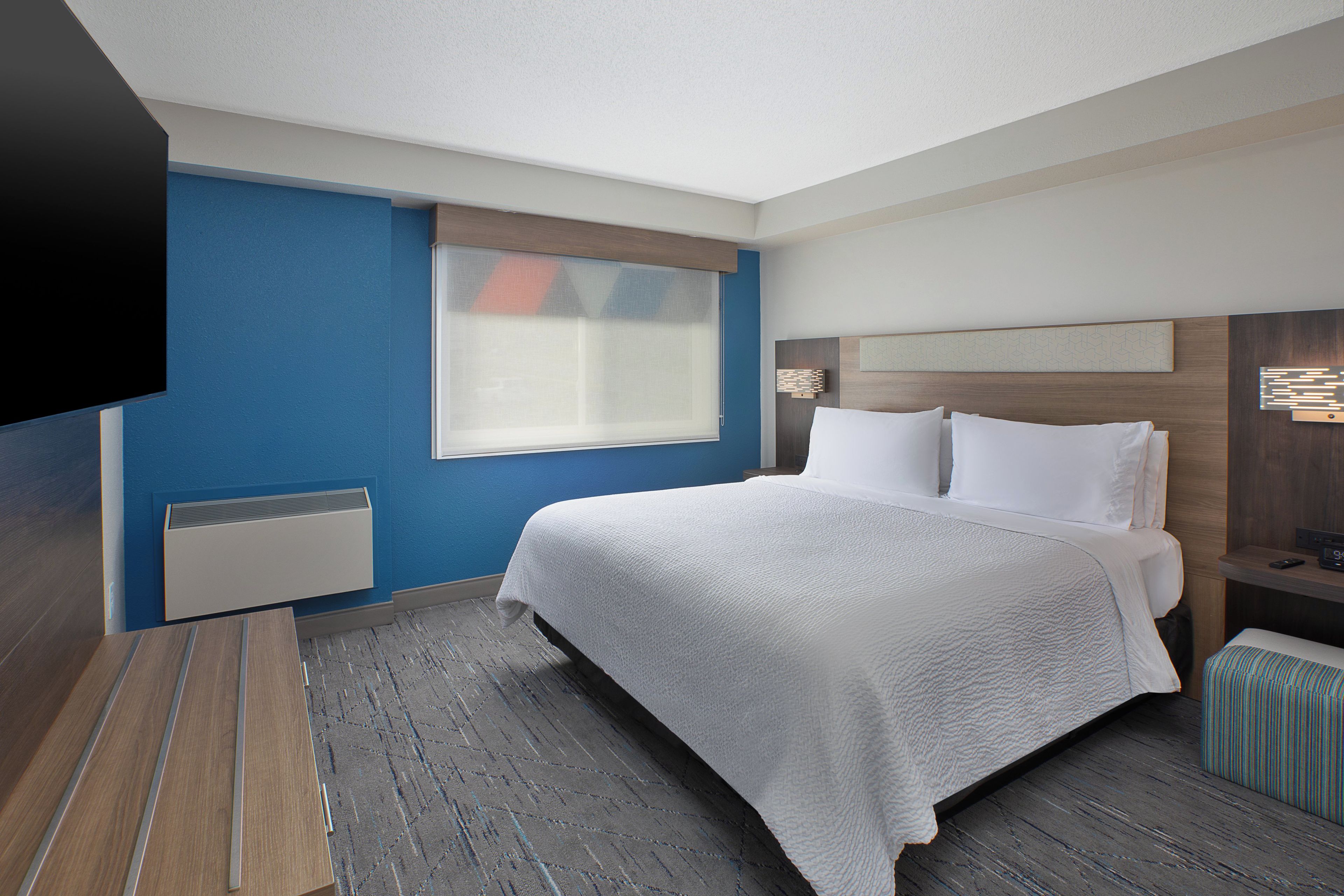 A hotel room with a large bed, a flat-screen TV, a bedside table, and a window with blinds.