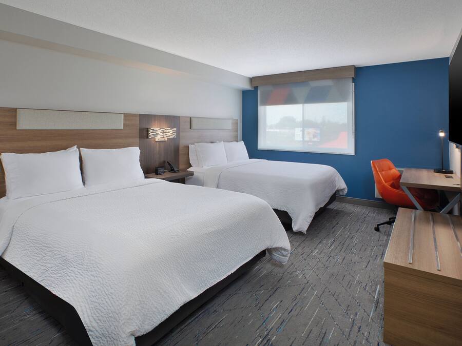 A hotel room with two beds, a desk, a chair, a TV, and a window.