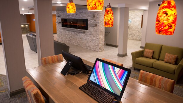 Un espace repas moderne avec un ordinateur portable posé sur une table en bois, une cheminée et un canapé en arrière-plan.