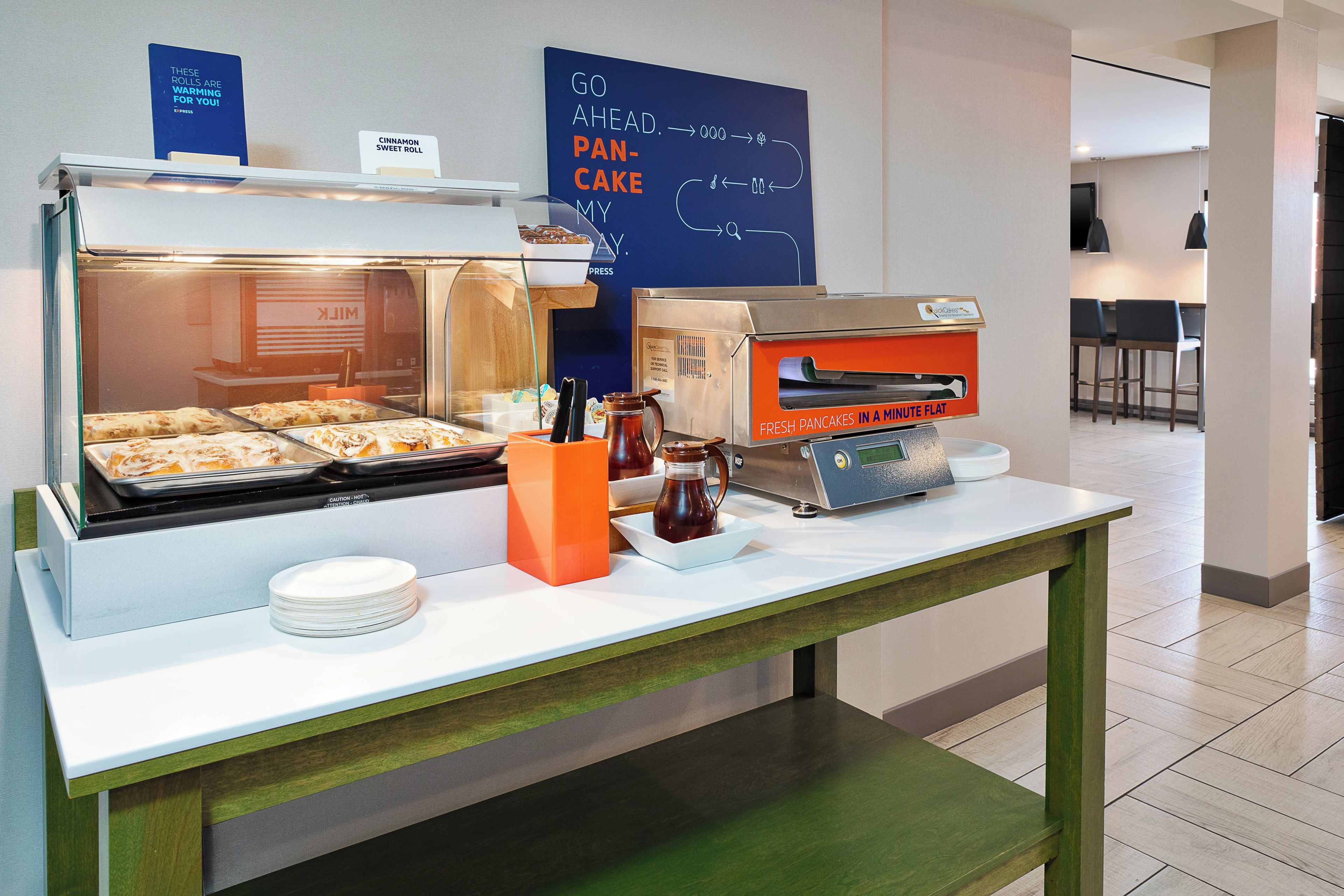 A breakfast buffet with a variety of food items, a coffee machine, and a sign indicating the availability of fresh pancakes.