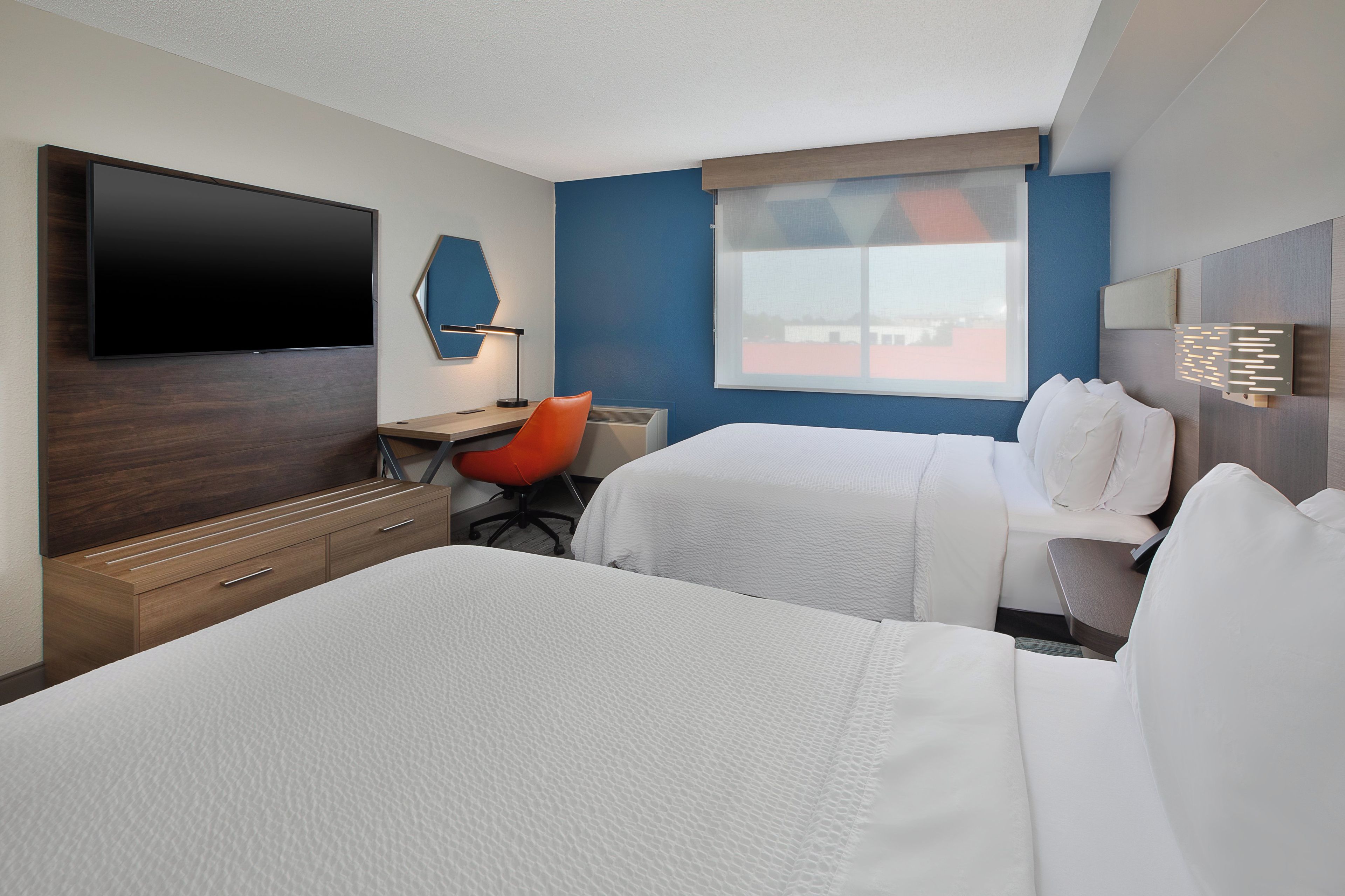 Une chambre d’hôtel équipée d’une télévision à écran plat, d’un bureau avec une chaise, de deux lits et d’une fenêtre donnant sur un paysage agréable.