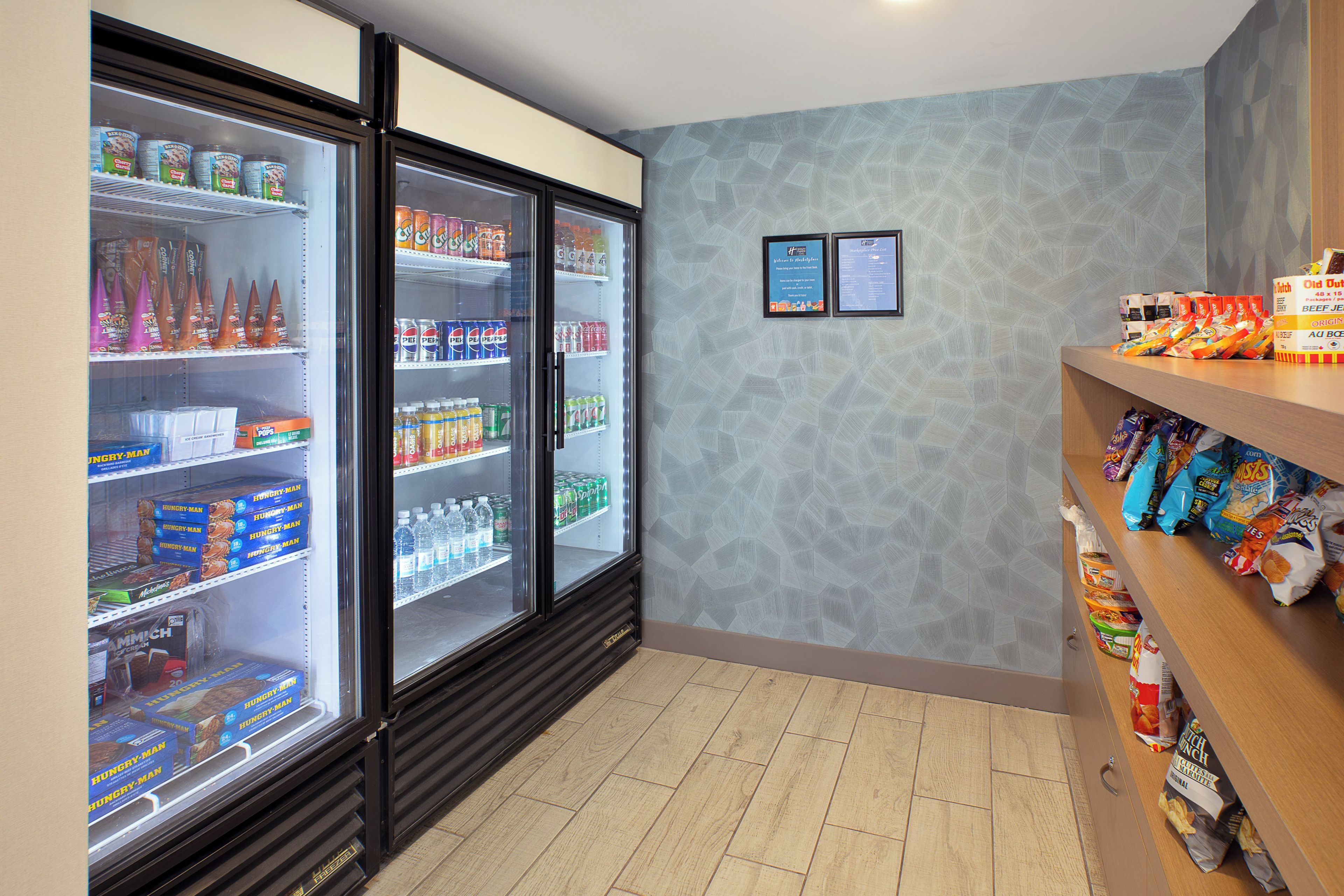 Un refrigerador exhibe diversas bebidas y aperitivos, una pared con carteles informativos y un mostrador con productos envasados.